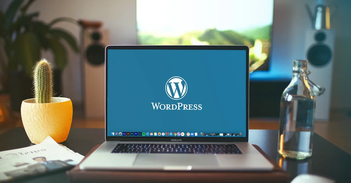 laptop showing wordpress logo on the table beside a cactus plant