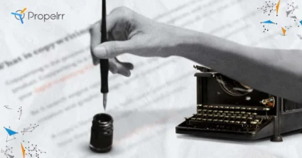 A typewriter behind a hand holding a quill above ink